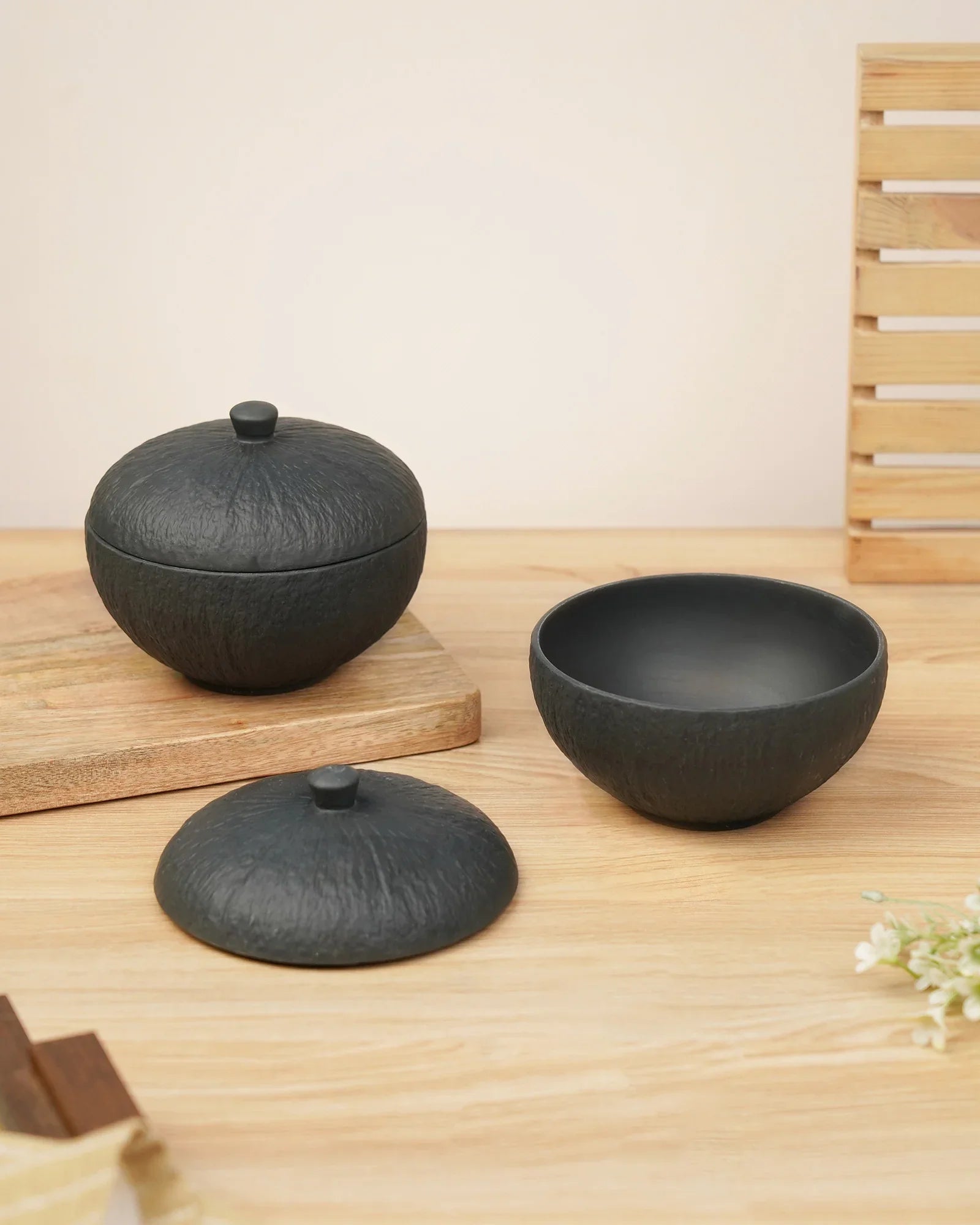 Black textured porcelain bowls with lids on a wooden table, premium Vola Global crockery.